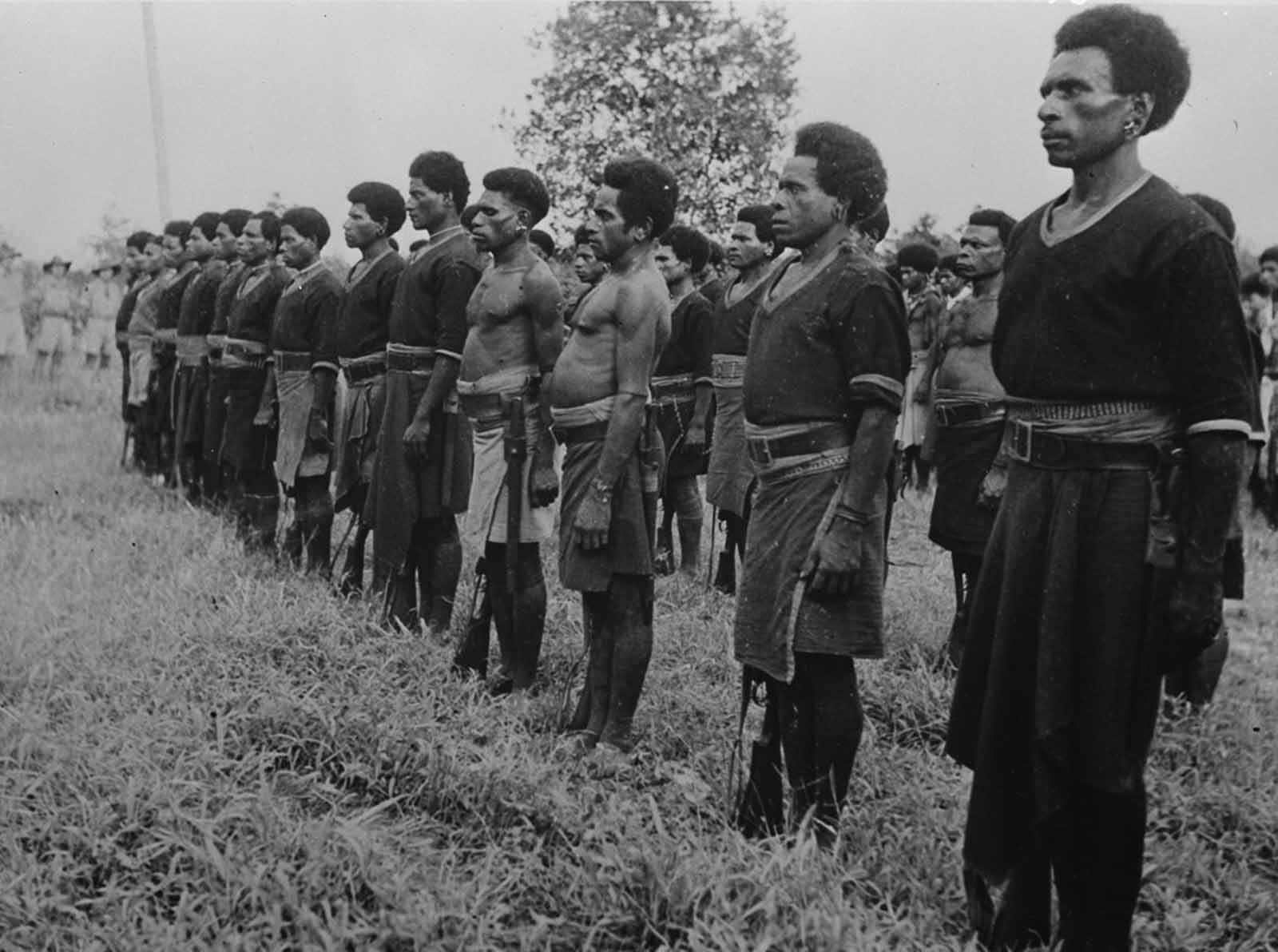 New Guinea police form an honor guard during a medal ceremony for native stretcher bearers and supply carriers.