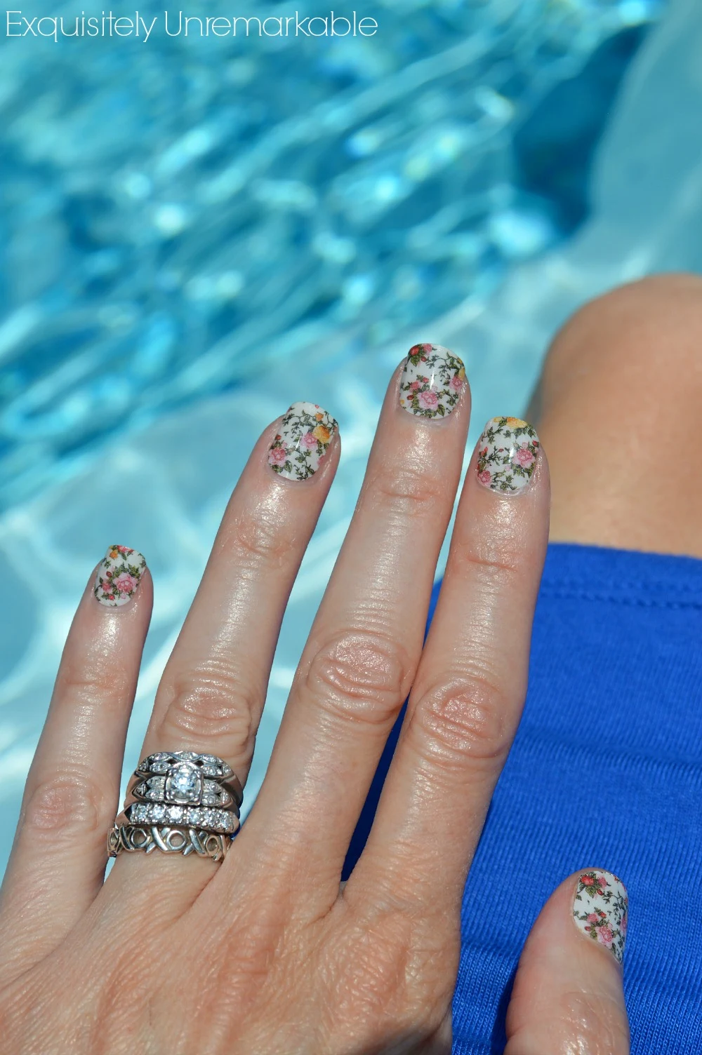 Hand in front of water wearing floral nail wraps