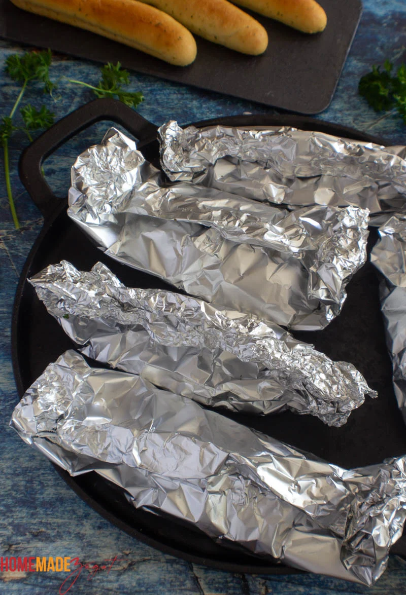 Baked foil packets of fish out of the oven on a black baking sheet.
