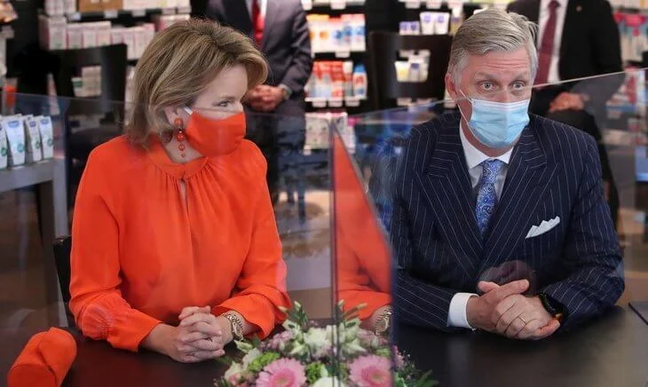 Queen Mathilde wore an orange color silk top and mask from Natan, and a beige wool coat by Natan. the pharmacy Pharma Haelvoet in Evere