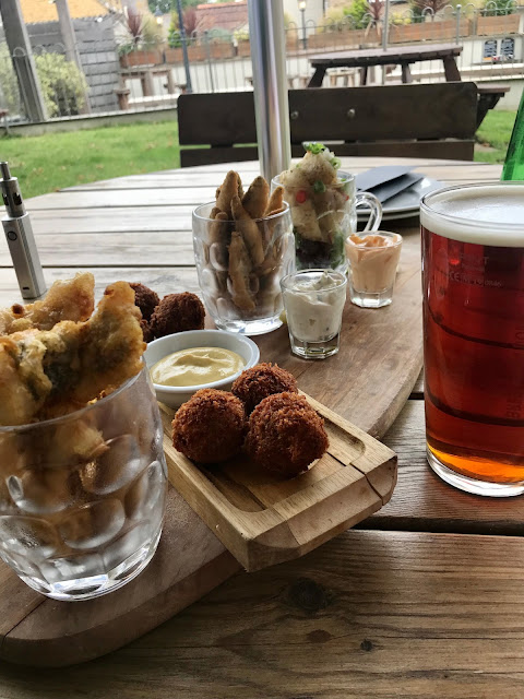A wooden board bearing several half-pint mugs full of fried food, and a pint of beer beside it