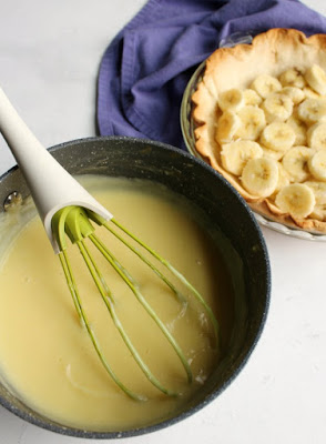 saucepan full of homemade vanilla custard in front of pie crust filled with banana slices