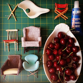 Selection of broken one-tweltfh scale modern chairs laid out next to a bowl of cherries and a tube of glue.