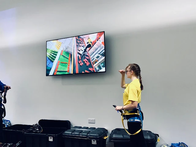 A TV screen with a video on and a member of staff in yellow top next to it
