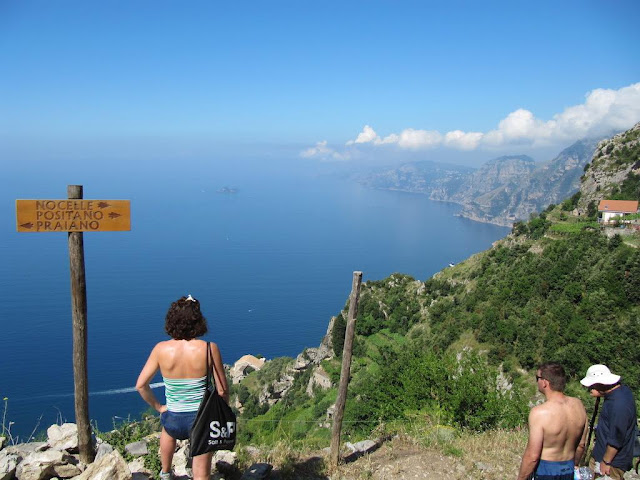 three tourists explore the nature trail overlooking the sea and are stopped to admire the breathtaking view of the Amalfi coast