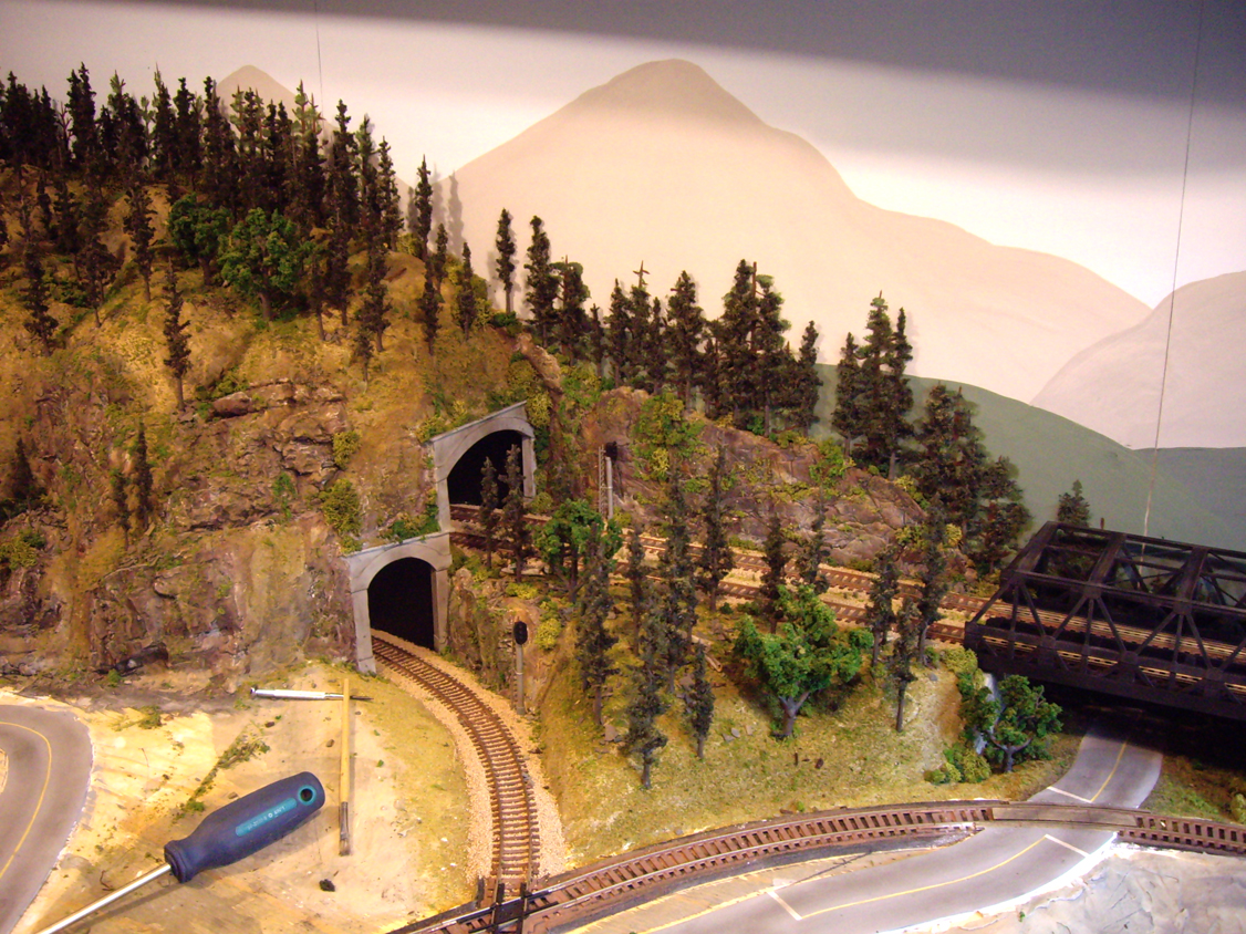 Completed mountain forest scenery between tunnel portals and a warren truss bridge