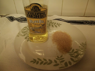 A bottle of Filippo Berio Olive Oil standing on a plate next to a pole of brown sugar. 