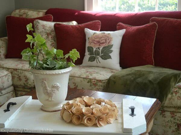 Cottage style floral couch with floral pillow, red pillows, floral wreath and ivy planter on tray.