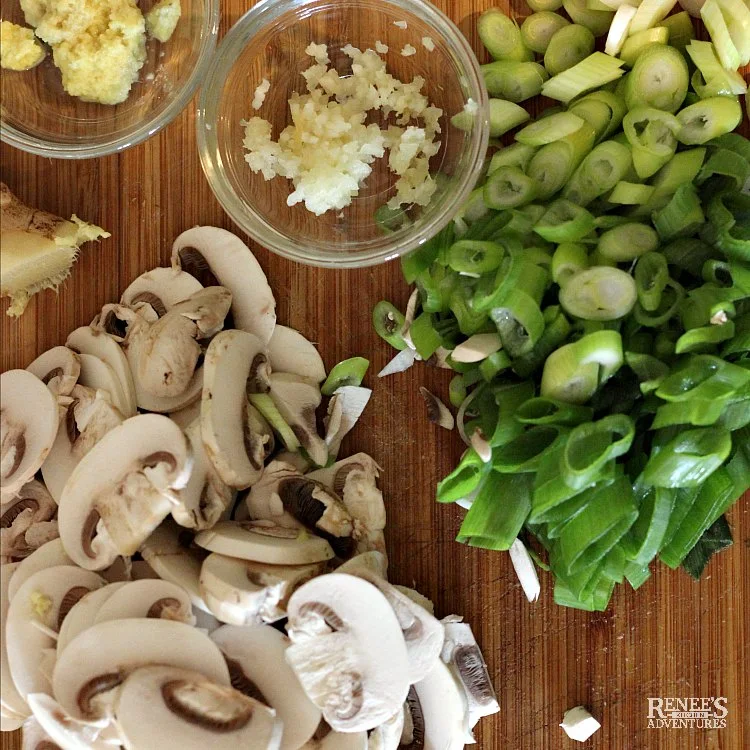 Overhead shot of ingredients (chopped mushrooms, garlic, ginger, scallions) on a wooden cutting board ready for Spicy Chinese Beef Noodle Soup by Renee's Kitchen Adventures