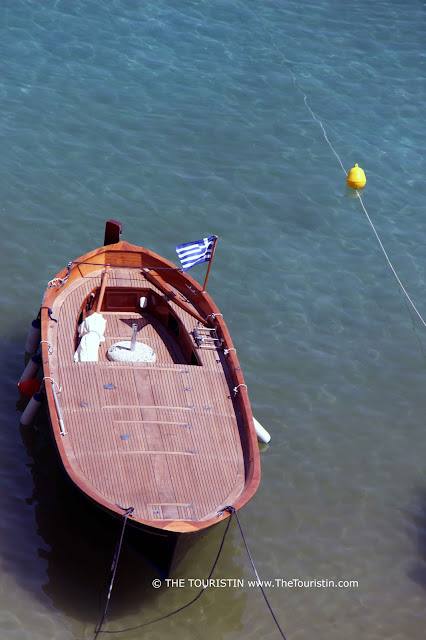 A travel guide to Lindos in Greece.The Touristin A wooden boat with a Greek flag, in the sea.