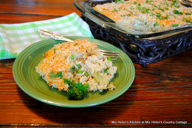This is a photo of a chicken and rice casserole served on a green plate with a fork, ready to eat. Behind the plate is the casserole in a baking pan. 
