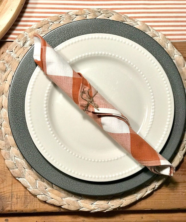 white plate and black charger with orange buffalo check napkin