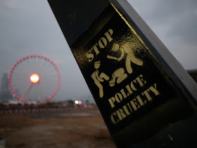"Stop Police Cruelty" graffiti on pedestrian bridge to Central Piers with the Hong Kong Observation Wheel in the background
