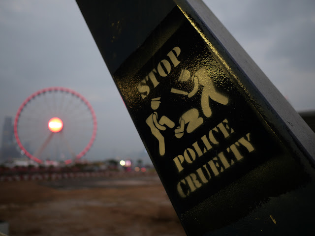 "Stop Police Cruelty" graffiti on pedestrian bridge to Central Piers with the Hong Kong Observation Wheel in the background