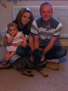 Mum dad baby in a family group sitting on floor with their German shepherd puppy.