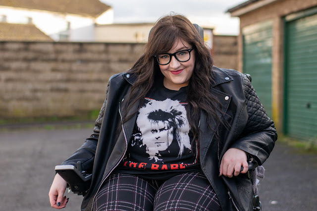 Woman sat in wheelchair wearing black leather jacket and tshirt with Bowie from Labyrinth 