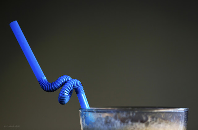 A Photograph of an Empty Cold Coffee Glass with a Twisted Blue Straw in it.