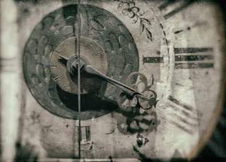 A black ad white photo of an old clock with roman numerals for numbers.