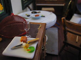 Modern dolls' house miniature post-party scene with empty serving platters and plates on tables.