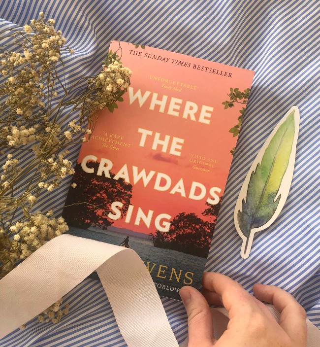 Top 10 books of 2020! Peach-pink front cover of Where the Crawdads Sing by Delia Owens next to a feather-shaped bookmark