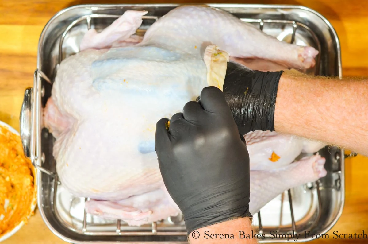A black gloved hand rubbing cajun herb butter rub under raw turkey skin.