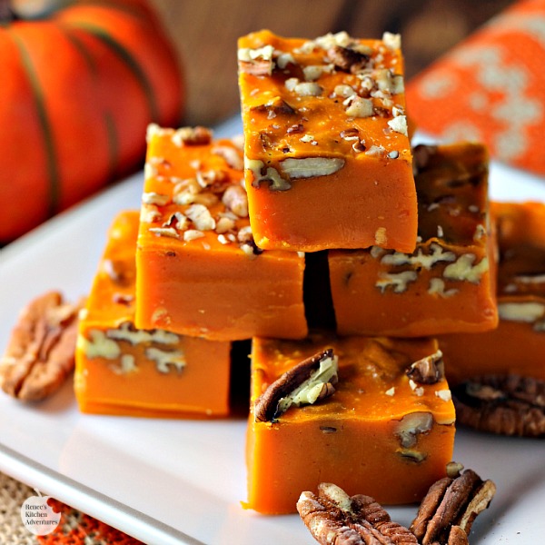 Easy Pumpkin Spice Pecan Fudge by Renee's Kitchen Adventures cut into pieces and on a white plate with pumpkin in the background.
