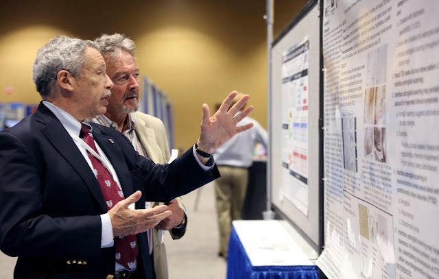 Dr. Dan Perl and a colleague look at a research board.