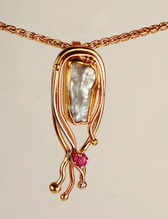 white flat pearl in pendant with squiggly wires and pink stone