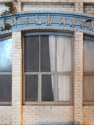 Window detail of a 1/24 scale model facade of an old three-storey commercial building with Chinese writing above it.