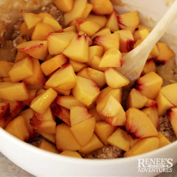 Peaches being folded into peach bread batter with wooden spoon