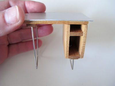 Hand holding a dolls' house miniature mid-century-modern desk in wood and metal.
