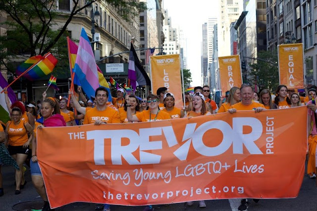 Image: The Trevor Project team holding up a sign of their logo in a Pride Parade
