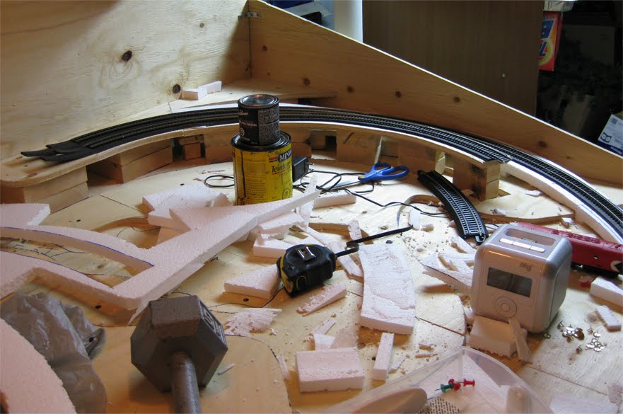 Benchwork covered in various construction materials with a section of completed track on foam roadbed