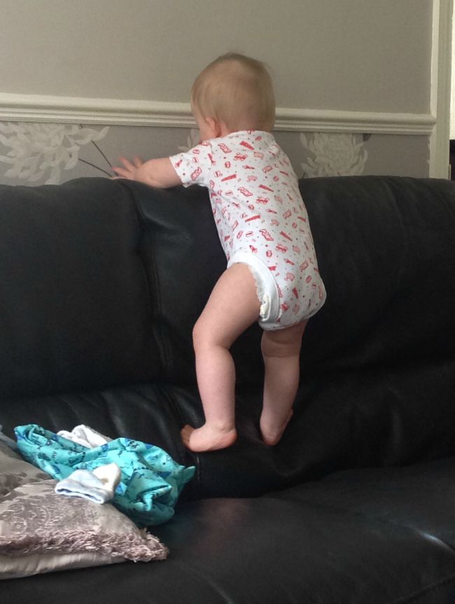 baby climbing the back of a black sofa