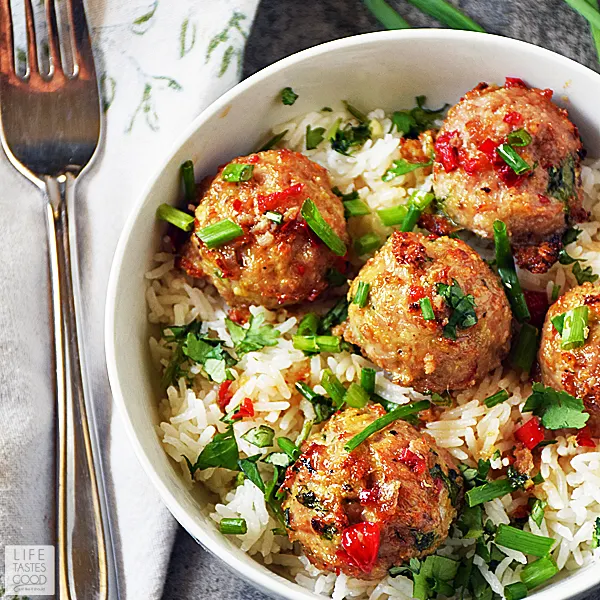Overhead view of Asian pork meatballs over creamy coconut rice in a white dinner bowl, garnished with chives.