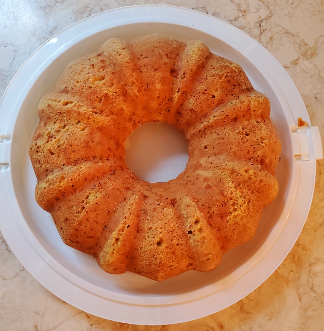 This is a bundt cake cooled and on the cake taker that is white made of plastic
