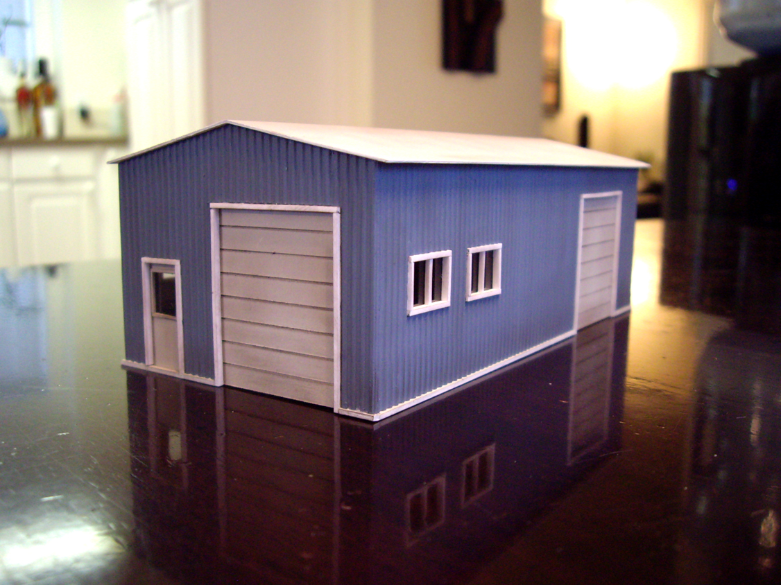 Scratch built styrene garage building with blue walls and white doors, windows, and roof