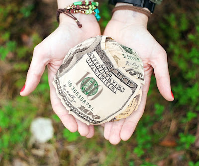 Dos manos abiertas, contienen sobre ellas, una cantidad de dinero en billetes, amontonados en forma de pelota.