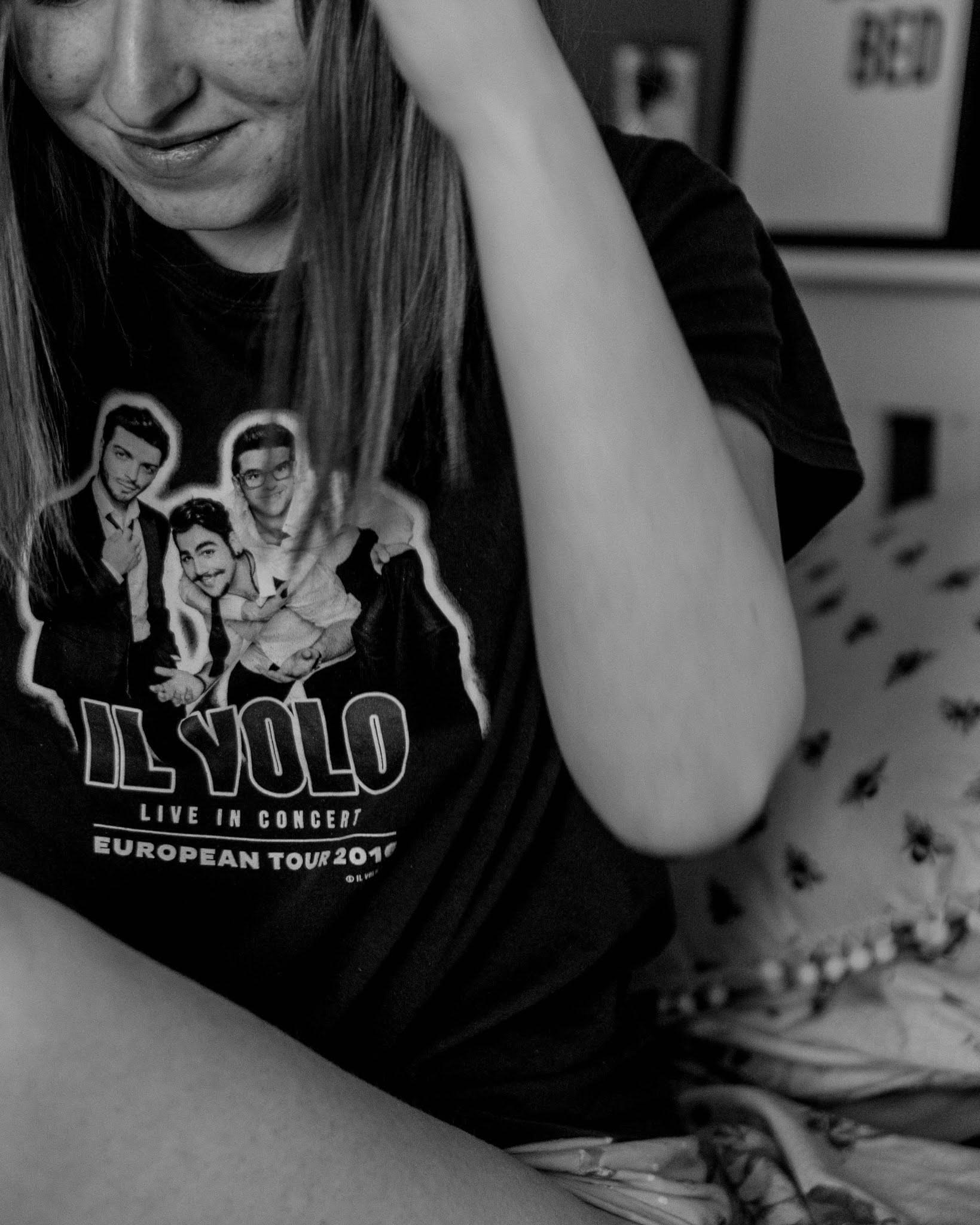 black and white photo of girl in il volo band tee sitting on bed