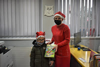 Bibliotekarka ubrana w czapkę Mikołaja wręcza dziecku książkę - prezent z okazji Mikołajek