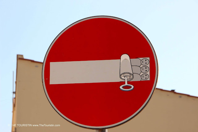 A sticker with three people lying in bed like sardines put on a regular No entry-street sign.