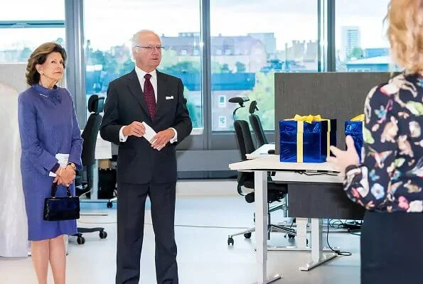 Queen Silvia wore and blue jacket and skirt, skirt suit. She is wearing gold earrings and gold bracelet