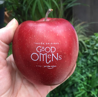 photo of a hand holding a red apple, on which appears the 'Good Omens' logo