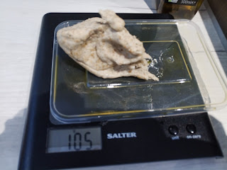 A ripped off piece of dough on a plastic lid on the scales, weighing 105g.