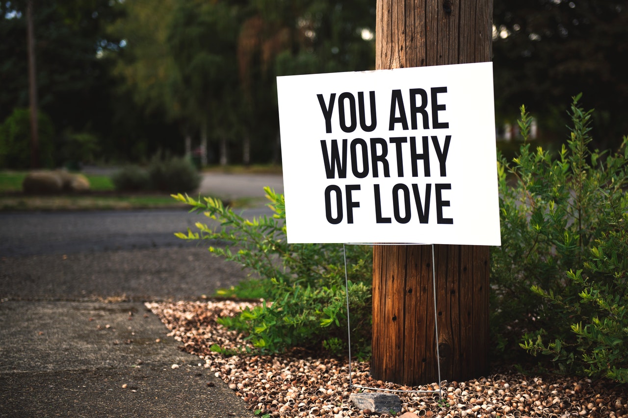 Practice self-care and self-kindness. Image containing a tree bark with a board on it with the text You are Worthy of Love
