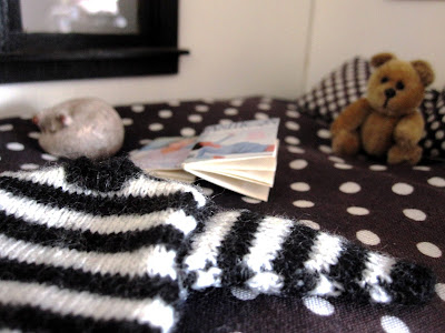 1/12 scale black and white striped jumper on a bed with a cat asleep in the background and a teddy bear propped up against the pillows.