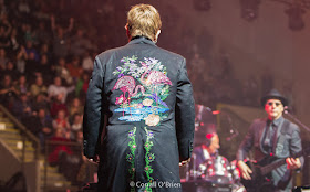Elton John acknowledges fans behind the stage. Image of Elton John with embroidered pink Flamingos on back panel of his jacket.