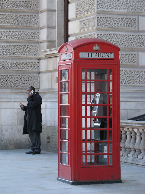 Мужчина разговаривает по мобильному телефону, стоя возле обычной телефонной будки, которая стоит пуста. Технологии, обеспечивающие мобильные телефоны, были впервые разработаны в 1940-х годах, но только в середине 1980-х они стали широко доступны.
