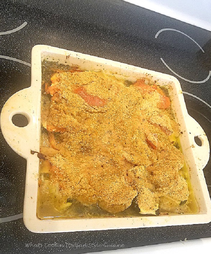 This is a baked cod fish on a white plate with a fall orange leaf basket in the background, a blue water glass and fork with napkin. The plate has a bed of spinach topped with baked cod fish with roasted vegetables on top along with bread crumbs toasted with Parmesan cheese and sliced tomatoes.