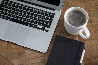 A laptop, beside a mug and notebook